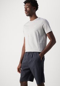 Tricou gri cu mânecă scurtă dintr-un material ușor, asociat cu pantaloni șort albaștri cu talie elastică și buzunare laterale, având o croială relaxată.