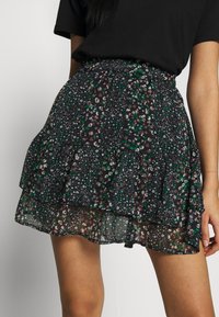 Mustaharjulle musta lillakoor, millel on kihilised volangid. Omab roheline ja pruun lillemuster läbipaistval mustal kangal. Nähtav elastne vöökoht.