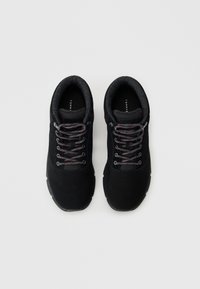 Zapatos de senderismo negros con un exterior de ante, cordones grises y un interior texturizado. El diseño cuenta con soporte para los tobillos y una suela acolchada.