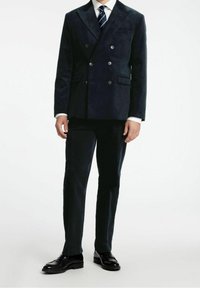 Marinblå dubbelknäppt jacka i mjukt tyg med knappar och fickor, i kombination med matchande byxor och svarta läderskor.