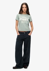 Lys grøn cropped t-shirt med hvid "SO.TRACK DEPT" print, parret med brede, mørke corduroybukser og mørkt fodtøj.
