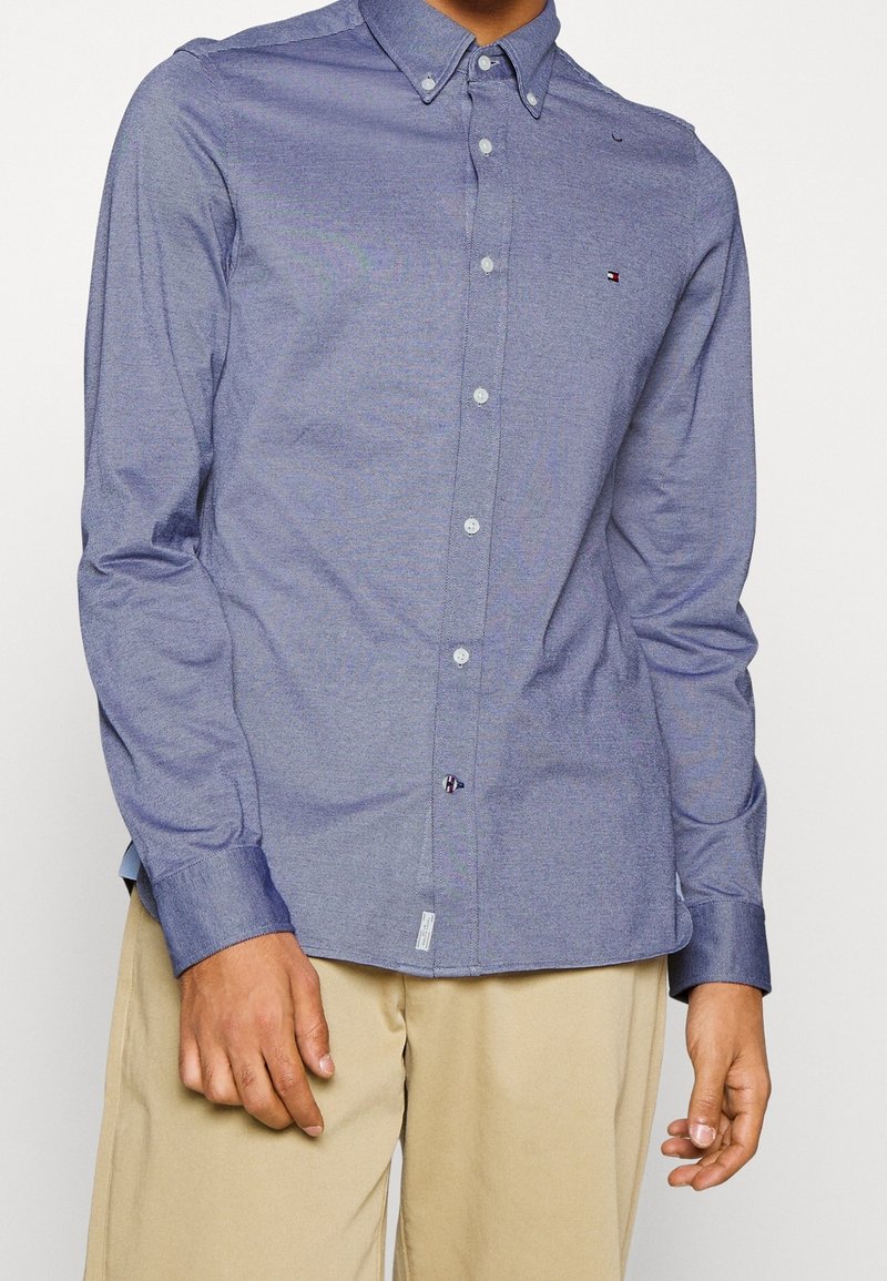 Camicia con bottoni a maniche lunghe in tessuto chambray blu scuro, con colletto, bottoni bianchi e un piccolo logo sulla tasca del petto.