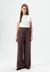 Wit T-shirt met korte mouwen gecombineerd met hoge taille, wijde broekspijpen in diep paars, met knoopdetail. Effen zwarte sokken zichtbaar.