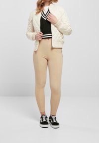 Chaqueta bomber acolchada color crema, suéter verde recortado con rayas blancas, leggings beige y zapatillas negras con suelas blancas.