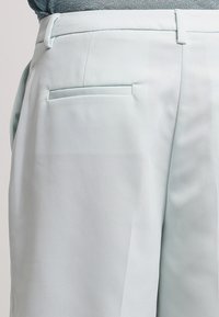 Ljusblå, skräddarsydda byxor i slät tyg, med en enda bakficka och hällor, designade för en smidig, modern passform.