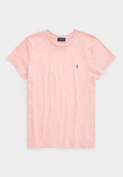 Camiseta de algodón de color rosa claro con un escote redondo y mangas cortas. Presenta un pequeño logotipo bordado en azul en el lado izquierdo del pecho. Textura suave.