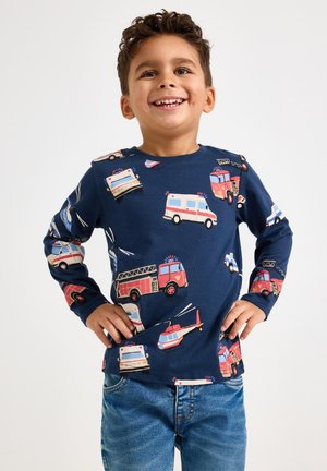 Laivastonsininen pitkähihainen paita, jossa on värikkäitä painokuvia hätäajoneuvoista. Pehmeä kangas, pyöreä kaula-aukko ja normaali istuvuus. Yhdistetty farkkuihin.