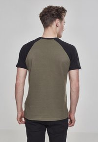 Tričko s krátkym rukávom v khaki farbe s čiernymi raglánovými rukávmi. Mäkká látka, okrúhly golier a klasický strih.