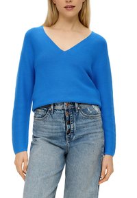 Blauer, strukturierten V-Ausschnitt Pullover mit langen Ärmeln, kombiniert mit hoch taillierten, hellen Jeans aus Denim mit Knopfverschluss und dezenten Used-Effekten.