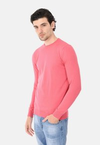 Maglione leggero e solido in corallo a maniche lunghe con un design aderente, realizzato in morbido tessuto a maglia, con polsini e orlo a coste.