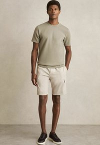 Lyse olivengrøn kortærmet t-shirt parret med beige shorts. Har en rund halsudskæring og sidelommer, suppleret med mørke sko.