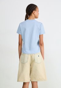 Ljusblå bomulls t-shirt med korta ärmar, tillsammans med beige denimshorts med en bakficka med logotyp.