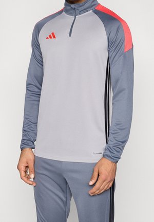 Mann trägt ein graues und hellgraues langärmeliges Sportoberteil mit orangefarbenen Akzenten und passende graue Hosen mit schwarzen Streifen.