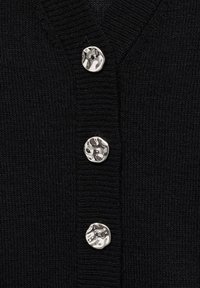 Cárdigan de punto negro con tres botones plateados brillantes y texturizados en una tapeta con detalles acanalados. Tejido suave con una textura lisa.
