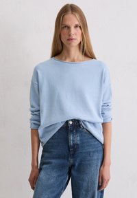 Hellblauer gestrickter Pullover mit weitem Ausschnitt und umgeschlagenen Ärmeln, kombiniert mit hoch taillierter blauer Jeans. Strukturierter Stoff mit lockerem Schnitt.