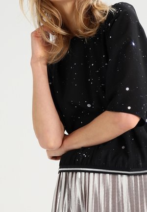 Blusa nera con motivo stellato, maniche corte e vita elasticizzata. Abbinata a una gonne plissettata argento metallico e bordature a strisce in contrasto.