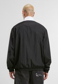 Veste légère noire avec une coupe décontractée, des poignets et un ourlet élastiques. Dotée d'un col blanc contrastant. L'arrière présente un détail de marque minimal.