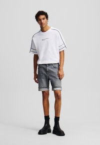 Camiseta blanca de manga corta con rayas negras; pantalones cortos de mezclilla gris con dobladillo doblado; botas negras hasta el tobillo. Textura de tela suave, diseño casual.