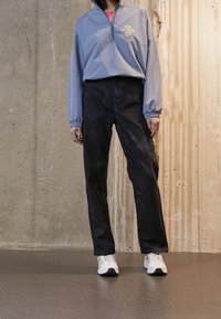 Light blue pullover with half-zip and logo, paired with black tapered pants and white sneakers. Smooth fabric with elastic cuffs.