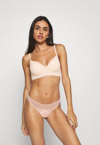 Bralet de culoare roz deschis, cu dantelă pe margini, cu bretele reglabile, dintr-un material neted, și un thong transparent asortat, cu detalii de broderie florală.