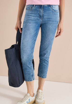 Personne portant un jean court bleu clair, des baskets blanches avec des accents bleus, et tenant un grand sac cabas bleu foncé.