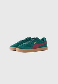 Adidași Puma din suede teal cu dungi maronii pe lateral și talpă din cauciuc natural, prezentați unul lângă altul pe un fundal alb.