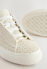 Baskets blanches tricotées avec une tige texturée, fermeture à lacets et semelle en caoutchouc dotée d'un motif en losanges. Embout lisse et col rembourré.