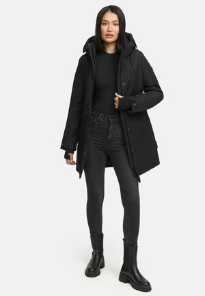 Zwarte capuchon parka met een rits aan de voorkant en drukknoopsluitingen, met een gevoerde binnenkant en zijzakken. Draag het over een zwart topje en jeans.