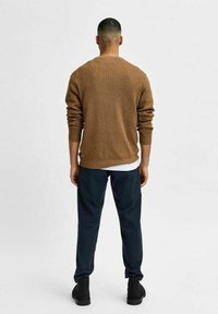 Ruskea neulottu pusero takaapäin nähtynä, yhdistetty tummiin ruudullisiin housuihin ja mustiin kenkiin. Puserossa on resorit kaula-aukon ja hihansuiden ympärillä.