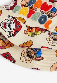 Eimerhut aus leichtem Stoff mit bunten Cartoon-Hundegesichtern mit verschiedenen Ausdrücken. "PAW PATROL"-Text in mehrfarbigen, gestickten Buchstaben.