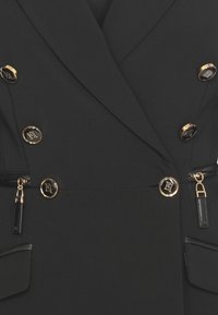 Blazer nero a doppio petto realizzato in tessuto liscio, con bottoni dorati con emblemi, tasche con zip e dettagli in pelle.