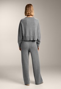 Grauer, gestrickter Pullover und Hosen-Set. Der Pullover ist cropped mit geripptem Saum; die Hosen sind weit geschnitten und an der Taille figurbetont. Weiche Textur.