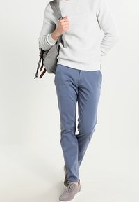 Ljust grårandig sweatshirt, blå byxor, grå mockaskor och en grå väska med bruna detaljer. Enkel design och modern passform.