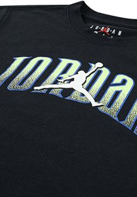 Camisa negra con un gran texto amarillento y azul que dice "JORDAN" y una silueta blanca de un jugador de baloncesto saltando con un balón.