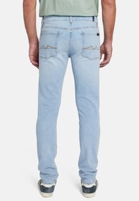 Jeans in denim blu chiaro con una vestibilità slim, dotati di due tasche posteriori con cucitura beige e una finitura pulita. Indossati con sneakers casual.
