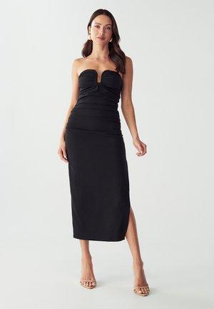 Robe noire sans bretelles avec fronces et une fente à l'avant, fabriquée à partir d'un tissu lisse, présentant un décolleté en cœur et une silhouette ajustée.
