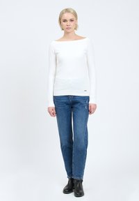 Witte lange mouwen top met een boot-halslijn, gecombineerd met mid-blauwe straight-leg jeans. Model draagt zwarte enkellaarsjes. Eenvoudig ontwerp, zonder patronen.