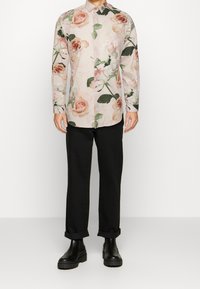 Camicia a maniche lunghe con bottoni floreale in rosa chiaro, con stampa di rose e foglie verdi; abbinata a pantaloni neri con risvolto e stivali neri chunky.