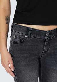 Black denim jeans with a faded finish, featuring a fitted design, front pockets, metal hardware accents, and visible stitching details.