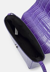 Fioletowa torebka z ekoskóry o fakturze krokodylej, prostokątnym kształcie i czarnym materiałowym wnętrzu. Otwarty górny brzeg odsłania szczegóły wnętrza.