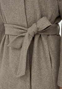 Páskový kabát z měkké, texturované, světle hnědé látky, s uzlovým páskem a zavinovacím designem.