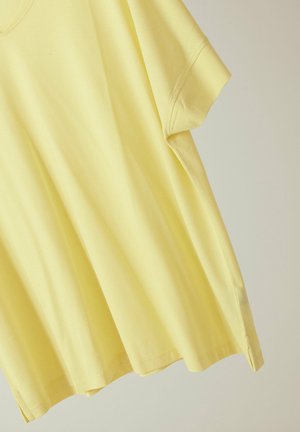 T-shirt en coton jaune clair à manches courtes avec col rond et fentes latérales sur un fond uni clair.