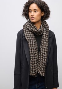 Sciarpa in misto lana con motivo houndstooth in nero e beige. Tessuto morbido, bordi frangiati, indossata in modo morbido attorno al collo.