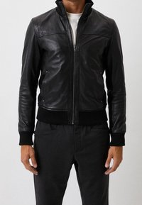 Svart läderjacka med hög krage, framzip-öppning och ribbade ärmslut och fåll. Slät textur med subtila sömnadsdetaljer.