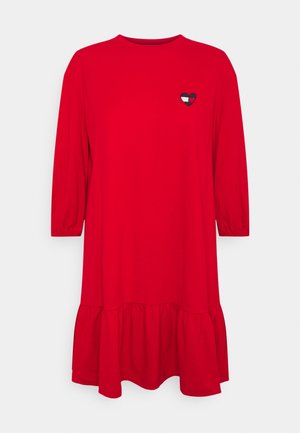 Czerwona sukienka do kolan z trzema ćwierć rękawami, falbaniastym dołem i małym logo w kształcie serca na górnej lewej części klatki piersiowej.