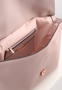 Borsa a tracolla in pelle rosa chiaro con una texture liscia. L'interno presenta una fodera chiara, con una tasca con zip dotata di un accento in oro rosa.