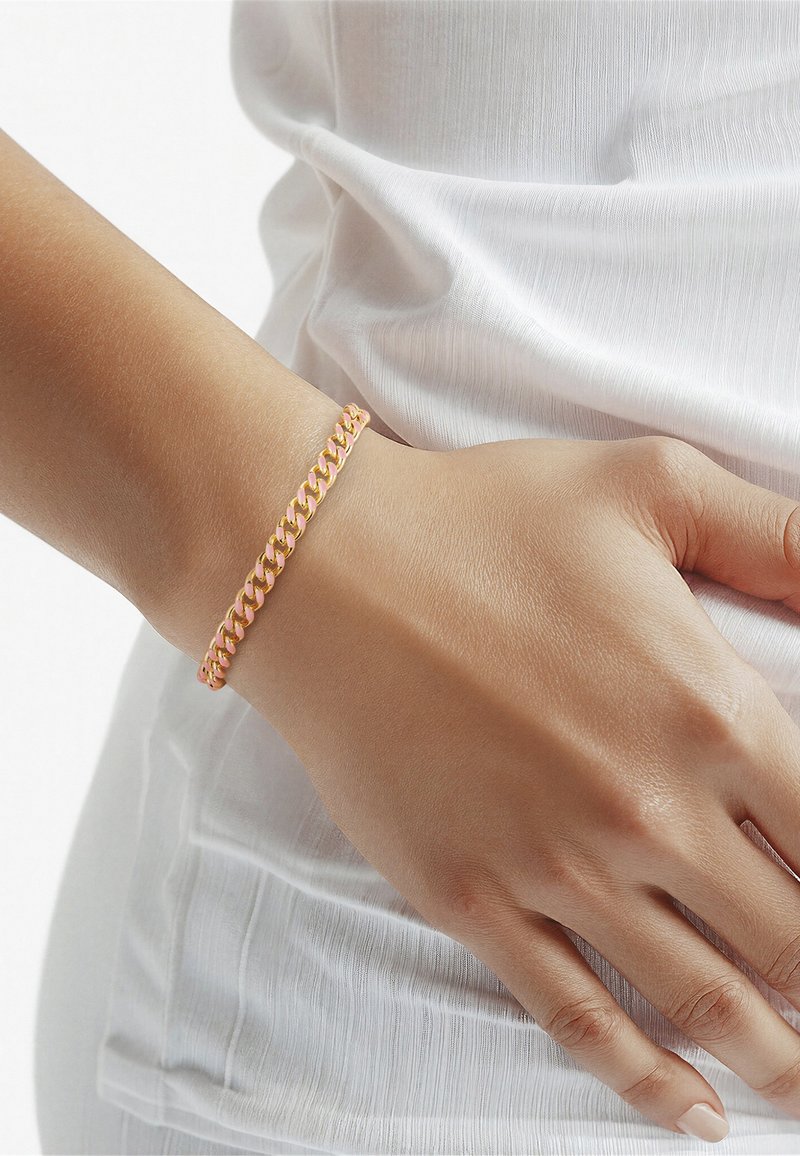 Primer plano de una mano apoyada sobre una superficie de tela blanca, que lleva una pulsera de eslabones dorada en la muñeca.