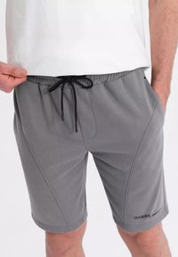 Shorts de sport gris avec une taille élastique à cordon de serrage, texture lisse, poches latérales et accents de couture. Logo de la marque visible sur l'ourlet.