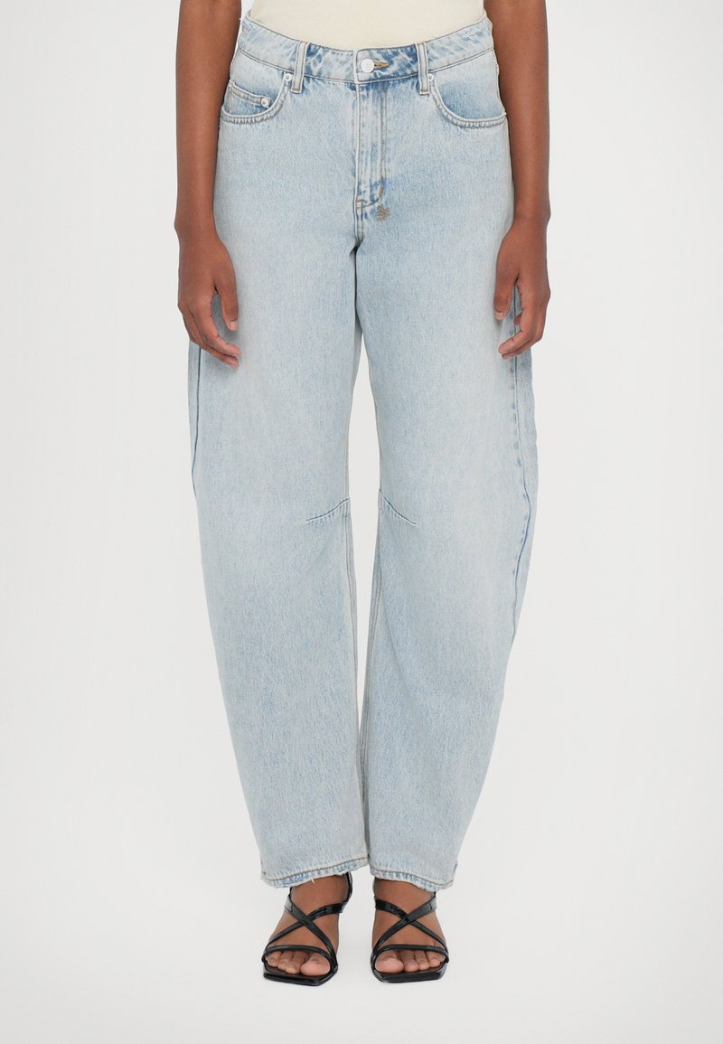 Lichtblauwe high-waisted jeans met een relaxte pasvorm, subtiele vervaging en voorzakken. In combinatie met zwarte sandalen met bandjes.