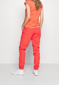 Korallinvärinen T-paita ja siihen sopivat korallinväriset juoksuhousut, joissa on joustavat hihansuut ja sivutaskut, yhdistettynä valkoisiin urheilukenkäisiin. Sileä tekstuuri.